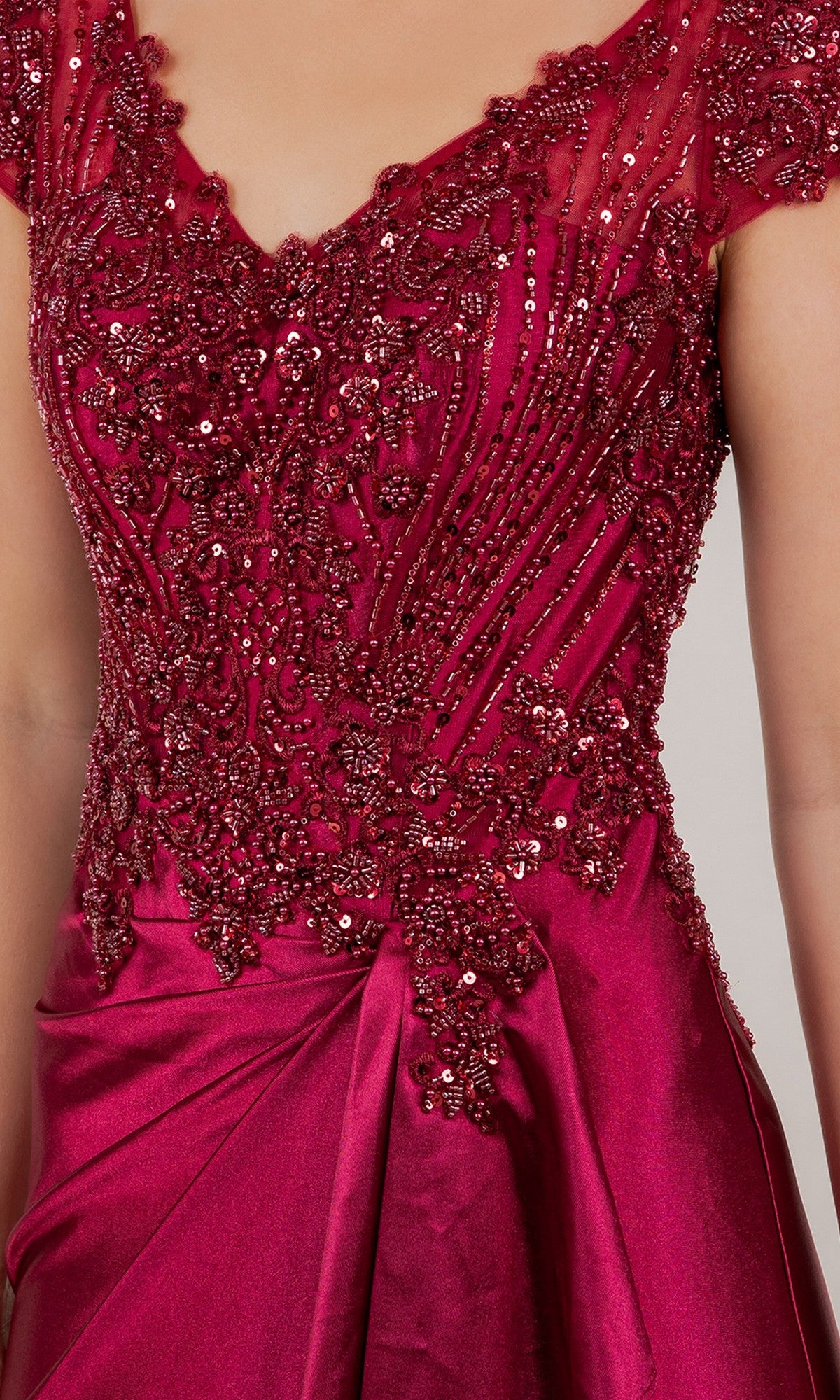 A close-up of a person wearing the Cinderella Couture 8513M long formal dress in magenta, featuring intricate bead and sequin embroidery on the bodice, cap sleeves, and a lustrous satin skirt.